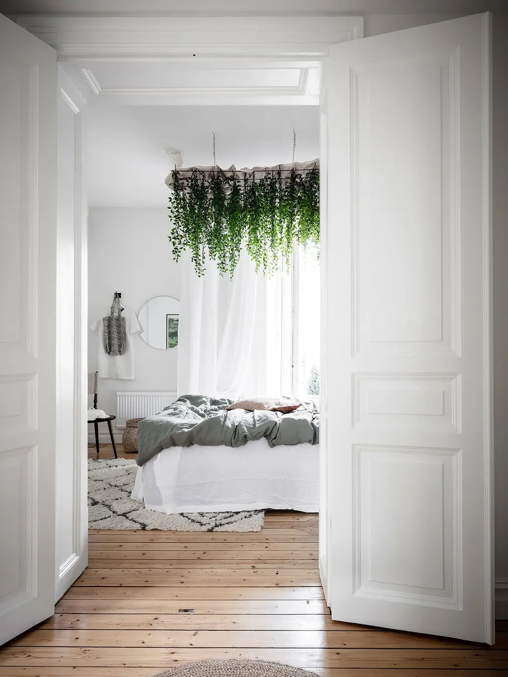 In deze fijne slaapkamer is een grote plantenrek aan het plafond boven het bed opgehangen.